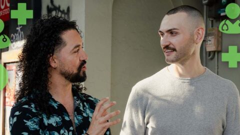 Colombian and white male couple walking on suburban street with green medical emojis around them
