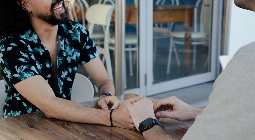 Colombian man with patterned shirt holding hand of date at a cafe