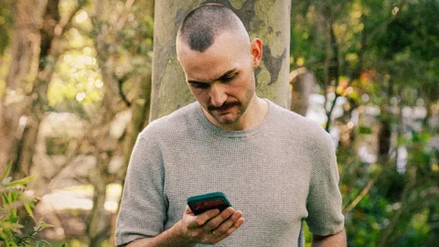 White man looking concerned at phone in park